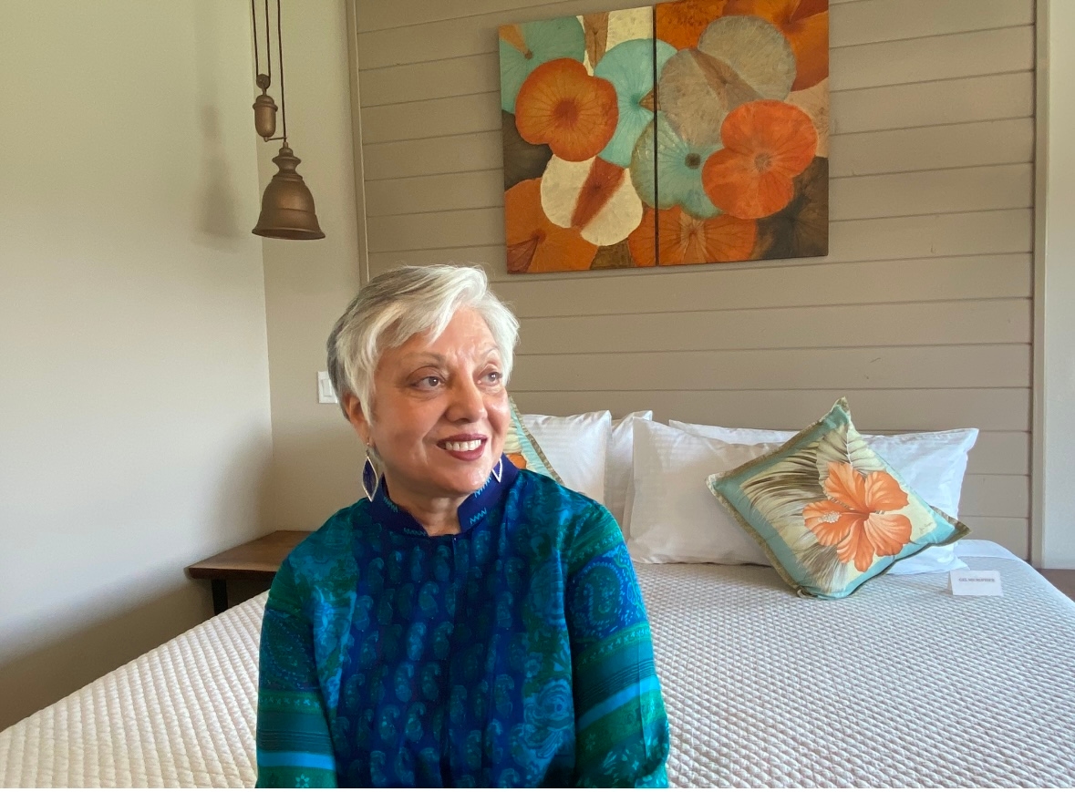 A woman sitting on the edge of a bed with colorful artwork on the wall behind