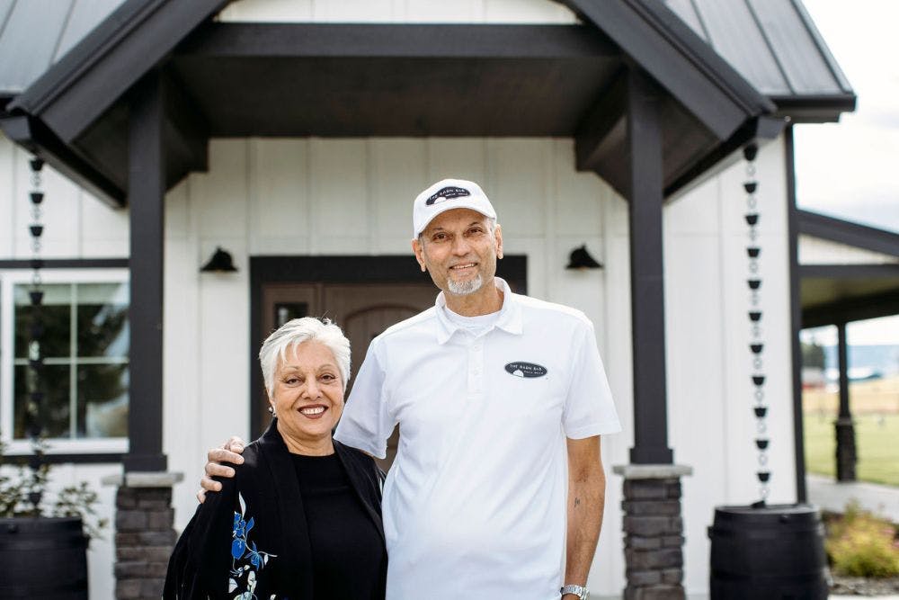 A man and woman standing together in front of a large white and brown home