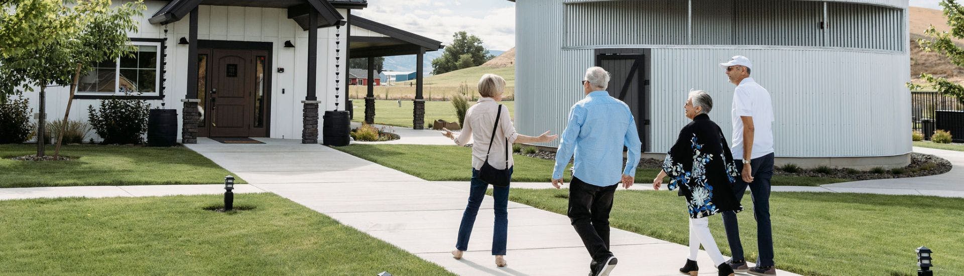 Two couples walking down a sidewalk in front of a large home and next to a silo