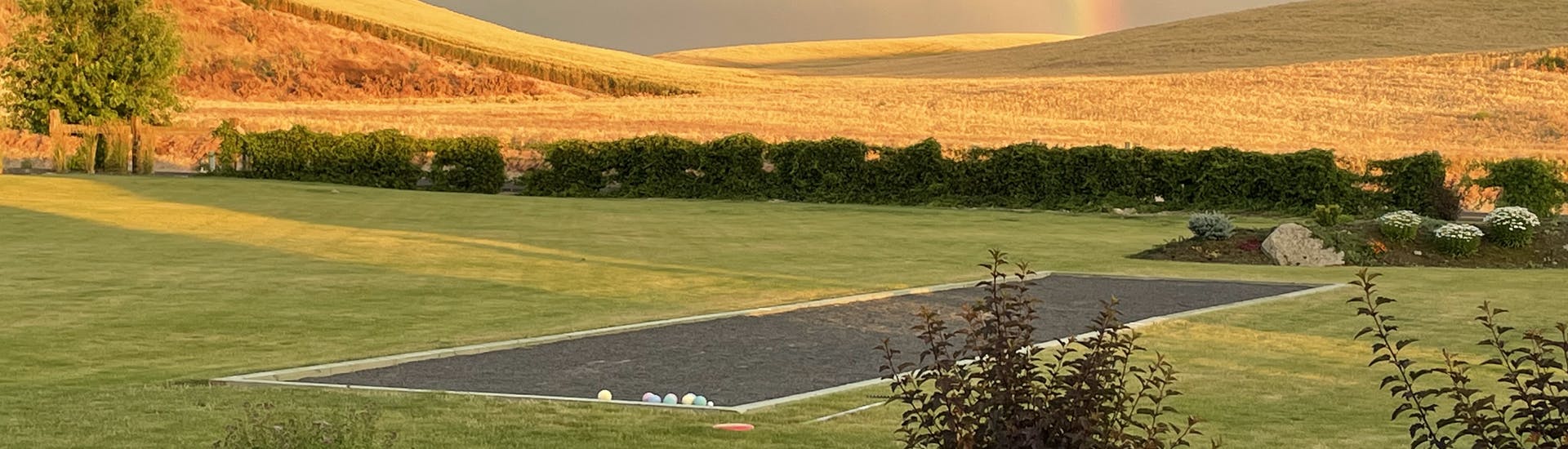 Bocce Ball Court in Green Pasture, with yellow wheat fields in the distance and a rainbow in the sky
