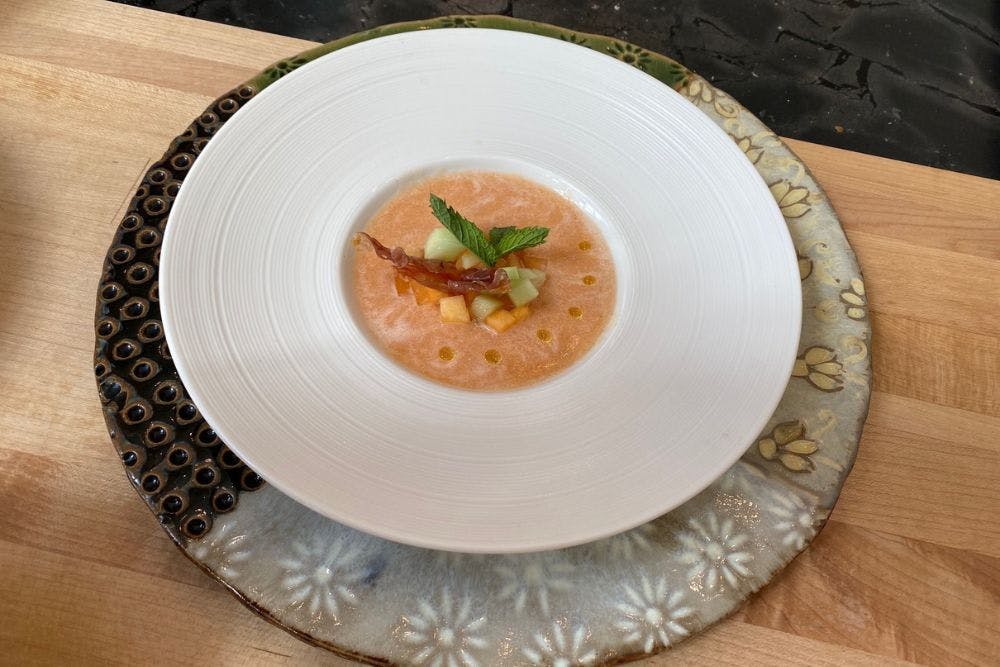 Large white plate filled with a cantaloupe soup on a colorful charger 