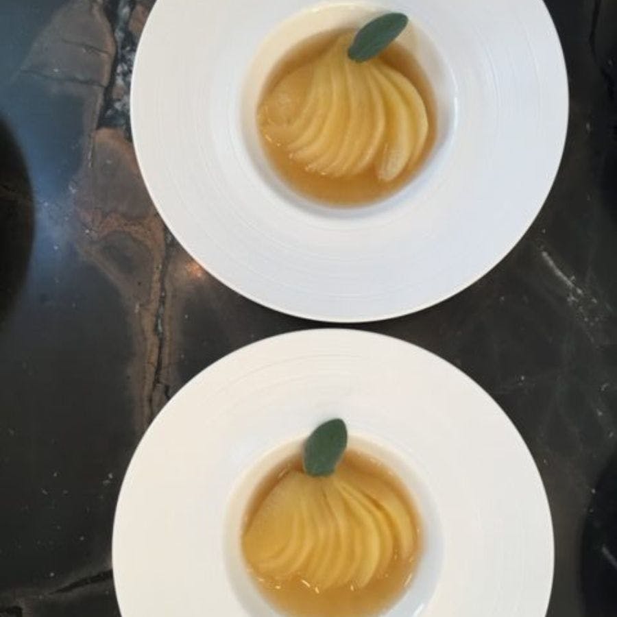 Two white round plates each with a sliced poached pear in a wine sauce with a spring of mint