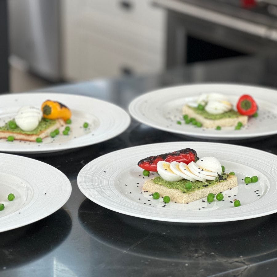 Four circular white plates with colorful gourmet food on a kitchen counter