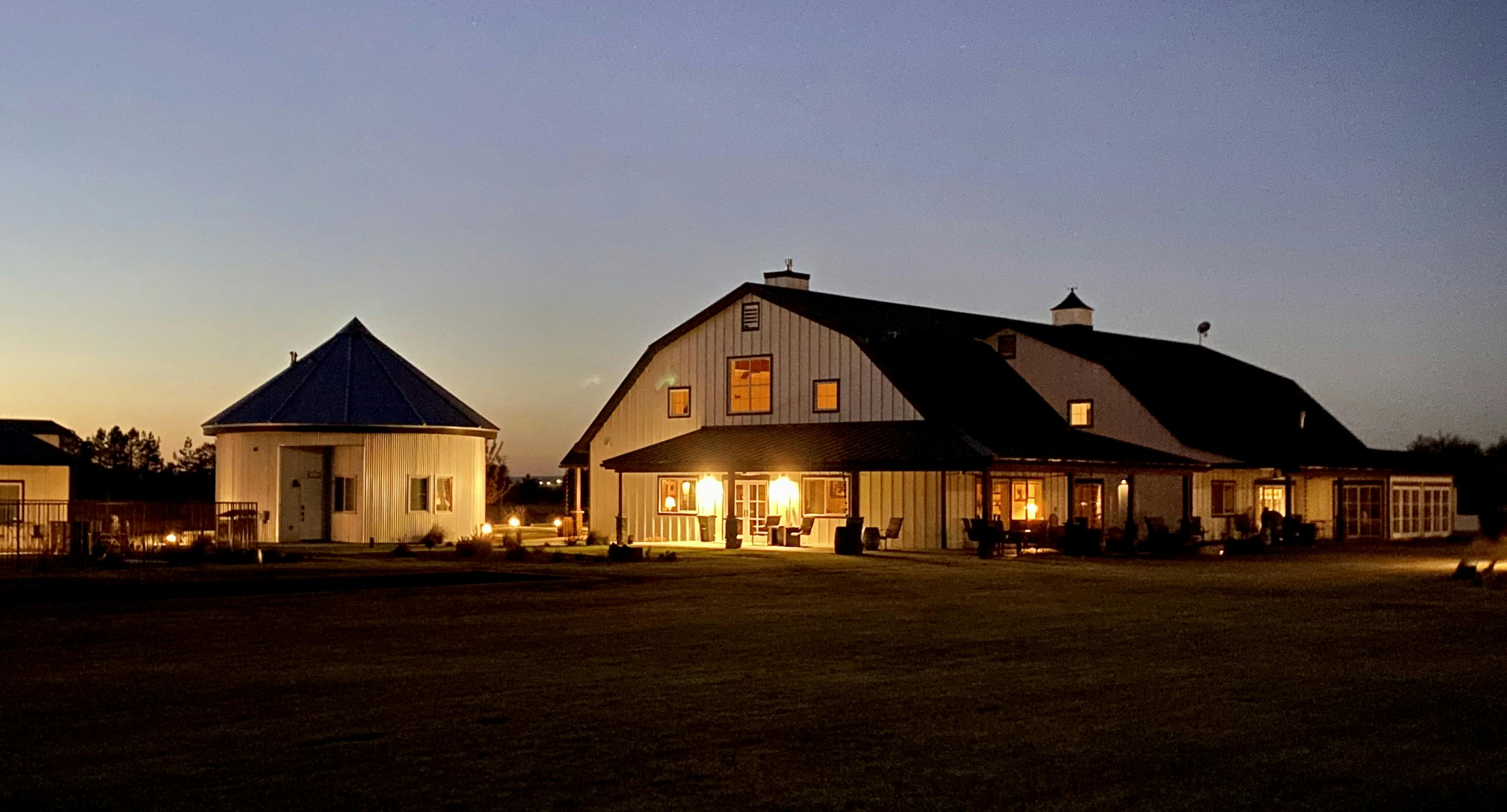 A large white barn and silo at night with golden glowing lights