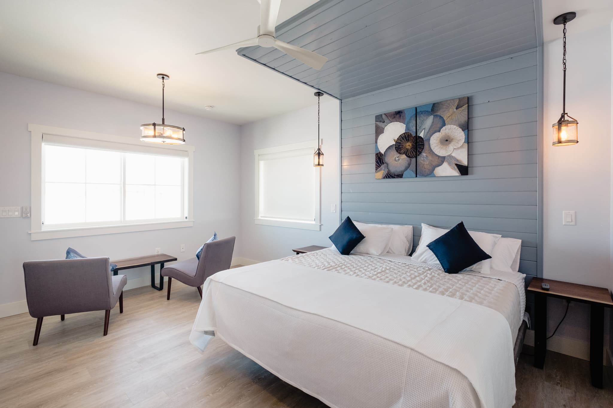 A view of the corner of the Vinifera Suite showing the pale blue wall, the live edge black walnut floating desk and chair. On the desk is the Nespresso coffee set up as well as a tea kettle and a selection of tea bags. In the bottom corner of the photo is the wine barrel that has been cut out to receive a mini wine fridge. On the top of the barrel is a bamboo tray with two stemless logo wine glasses and a corkscrew. The floor is grey laminate plank.