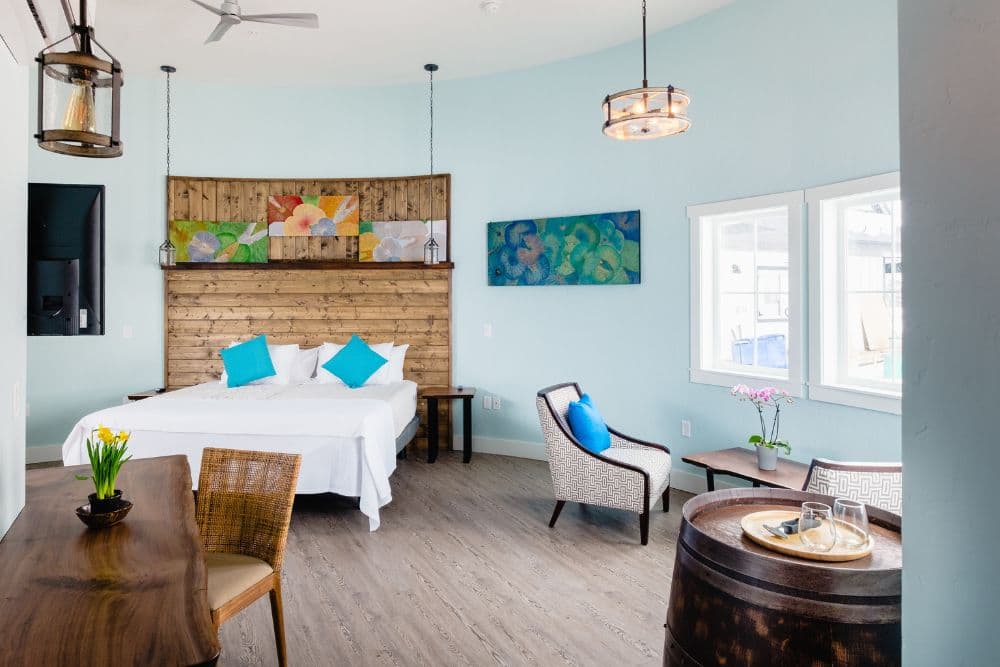 Large and spacious bedroom with wood feature behind bed, table with two chairs, wine barrel and large windows