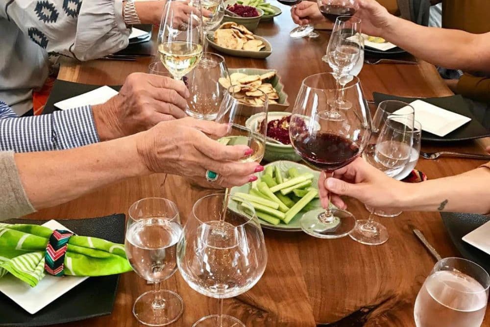 A group of people sitting at a dining table toasting their wine glasses together