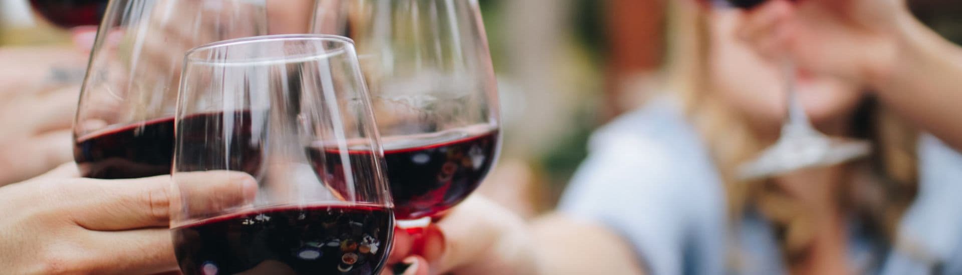 A group of people holding up and toasting three glasses of red wine