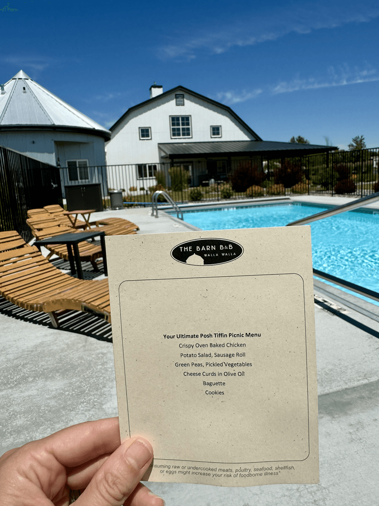 A hand holding up a small piece of paper with a menu by an outdoor pool with lounging chairs