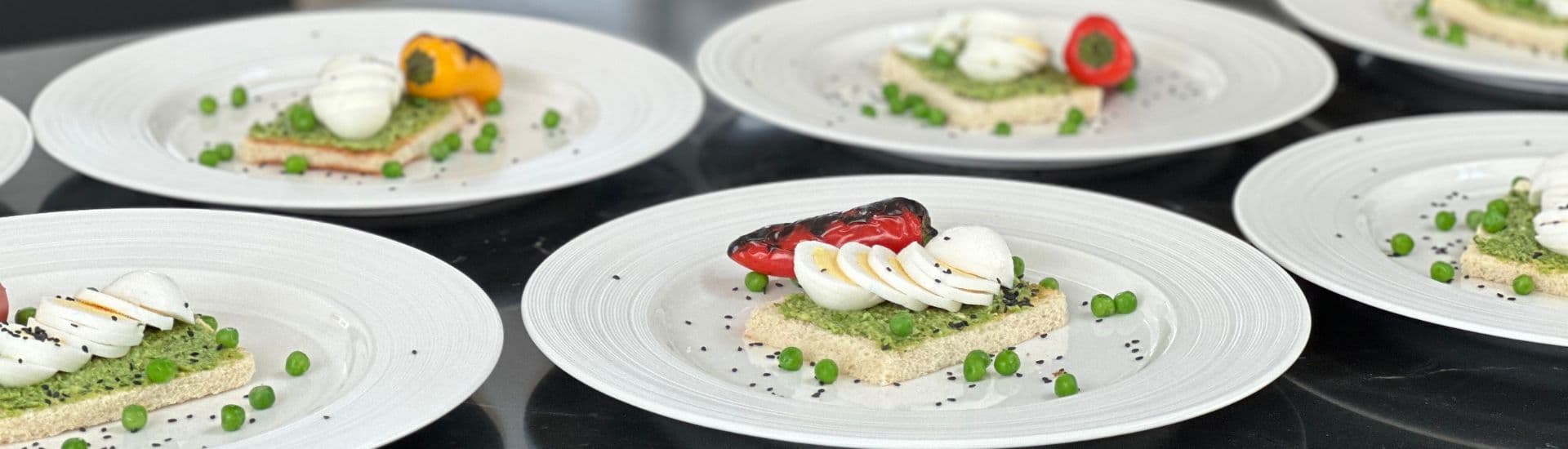 Several round white plates with a gourmet dish of toast, peas, sliced hard boiled egg and charred bell pepper