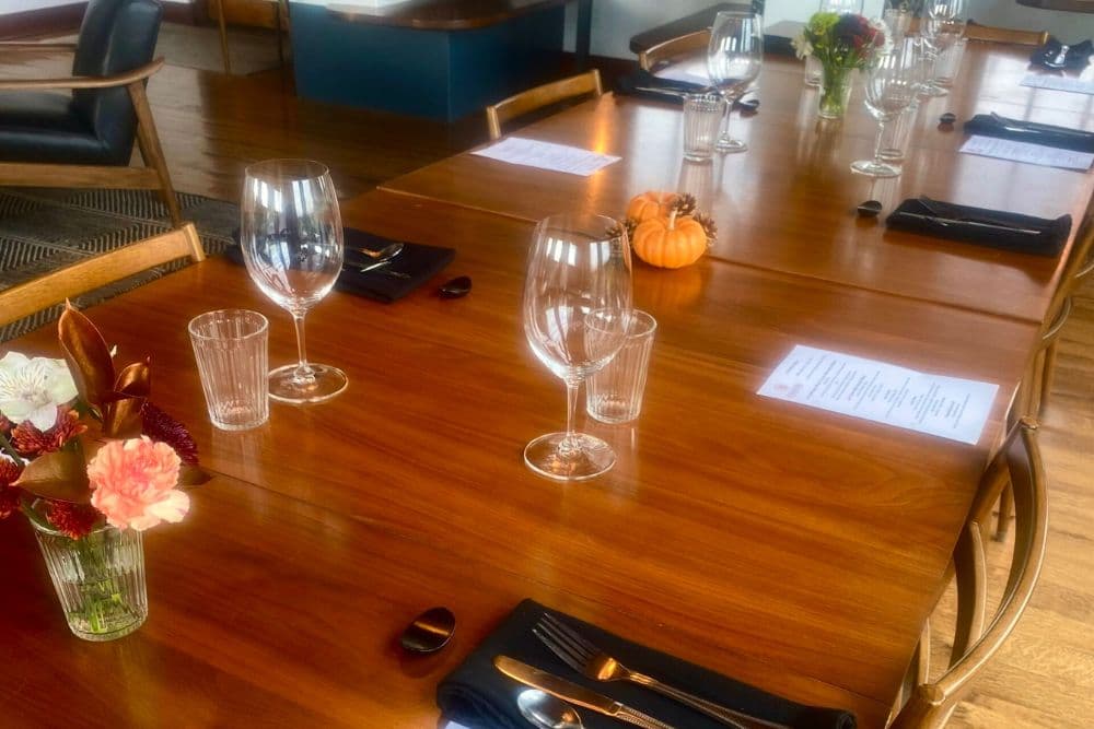 Restaurant tables with silverware over black napkins, wine glasses and vases of flowers