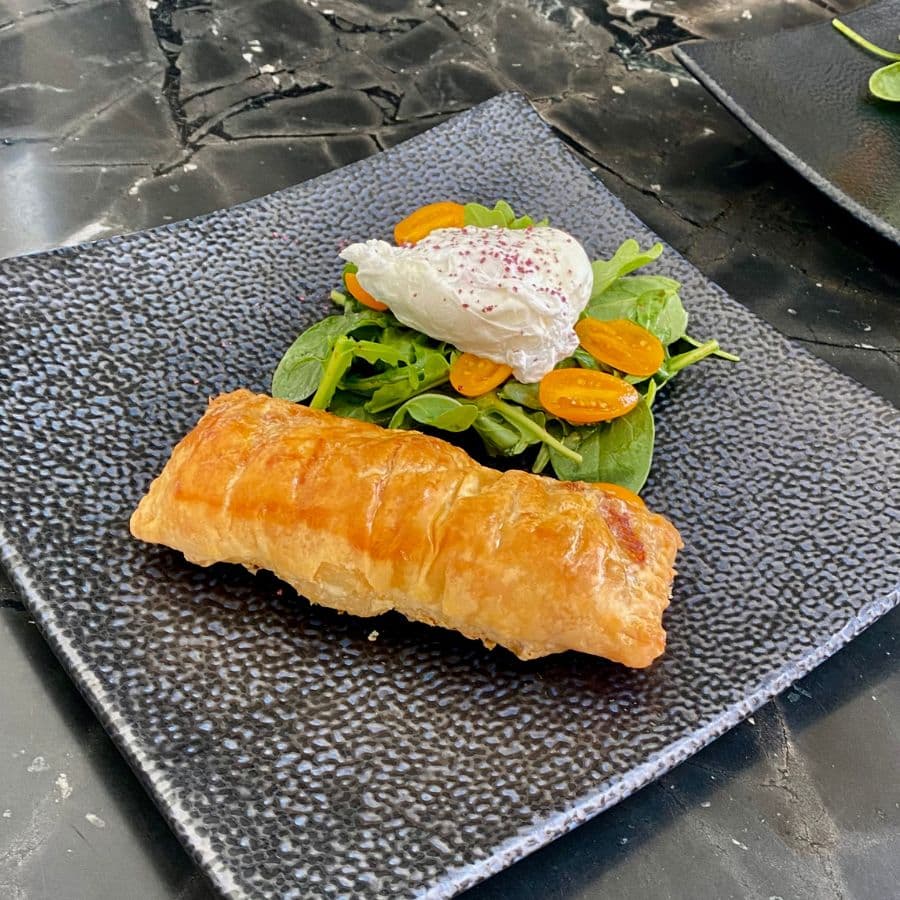 Square black plate with a golden brown meat puff and a side salad