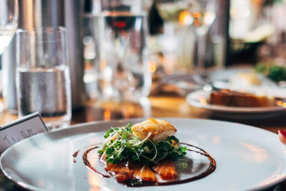 A restaurant dining table with a large white plate of elegant food, wine glasses and water glasses