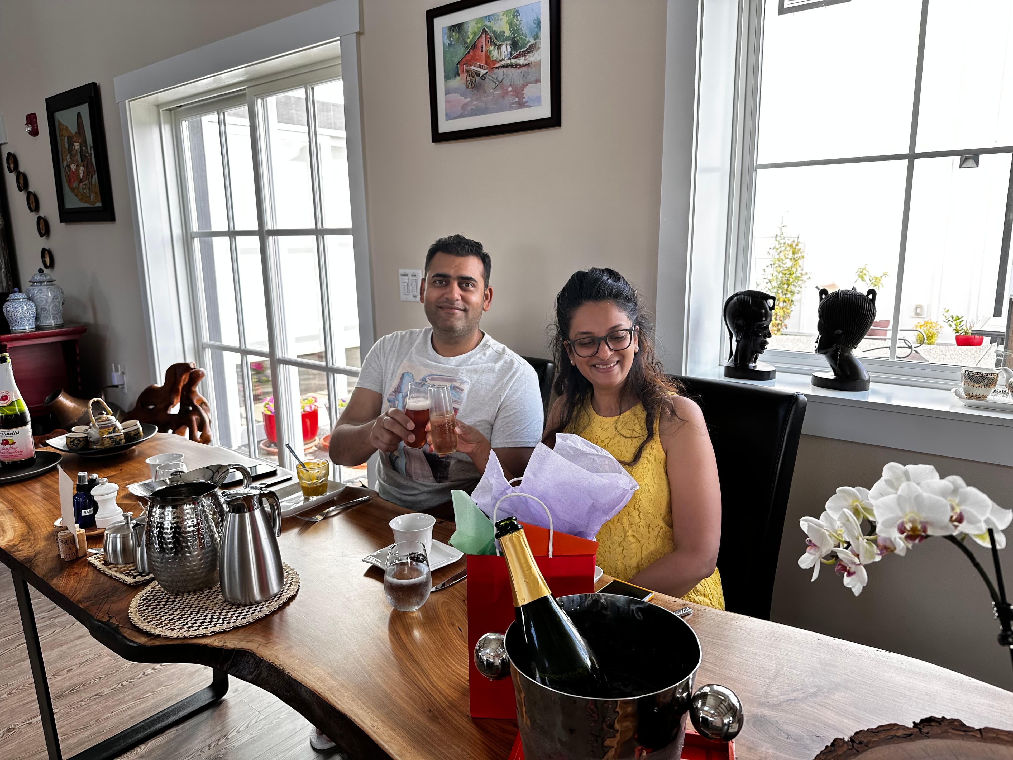 A man and woman enjoying drinks at a long live edge walnut table by large windows