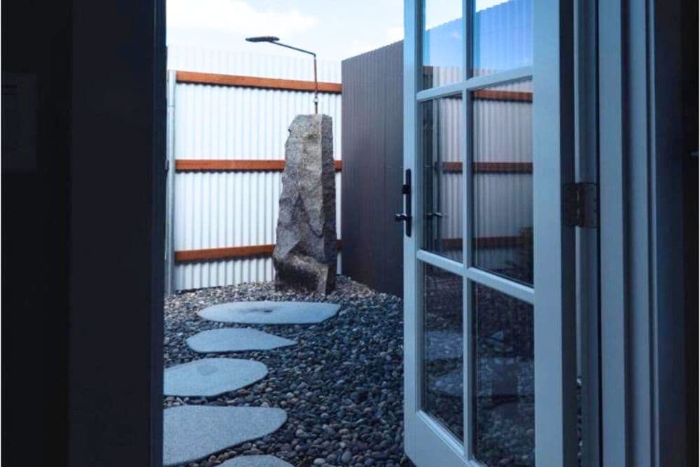 A unique outdoor shower in a fenced yard with a stone path